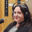 A woman with shoulder length brown hair. She has red lipstick on along with radio headphones.