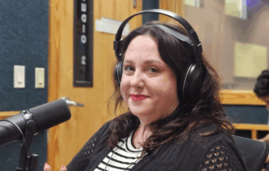 A woman with shoulder length brown hair. She has red lipstick on along with radio headphones.