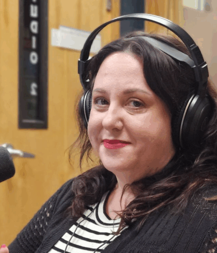 A woman with shoulder length brown hair. She has red lipstick on along with radio headphones.